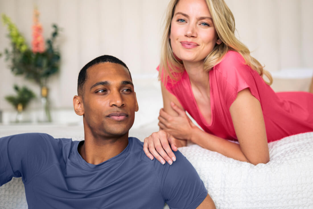 Man and woman sitting on a bed in a bedroom setting